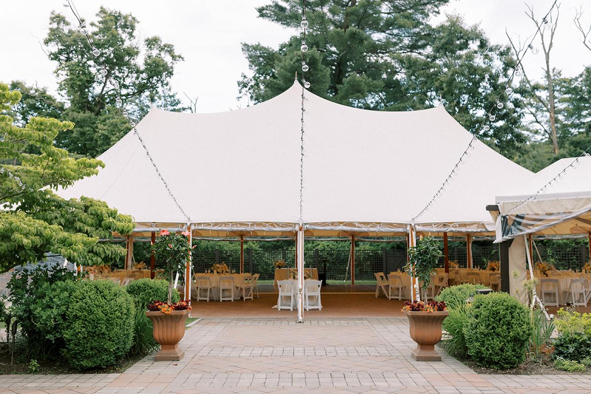 White outdoor tent with chairs and plants in a garden setting.