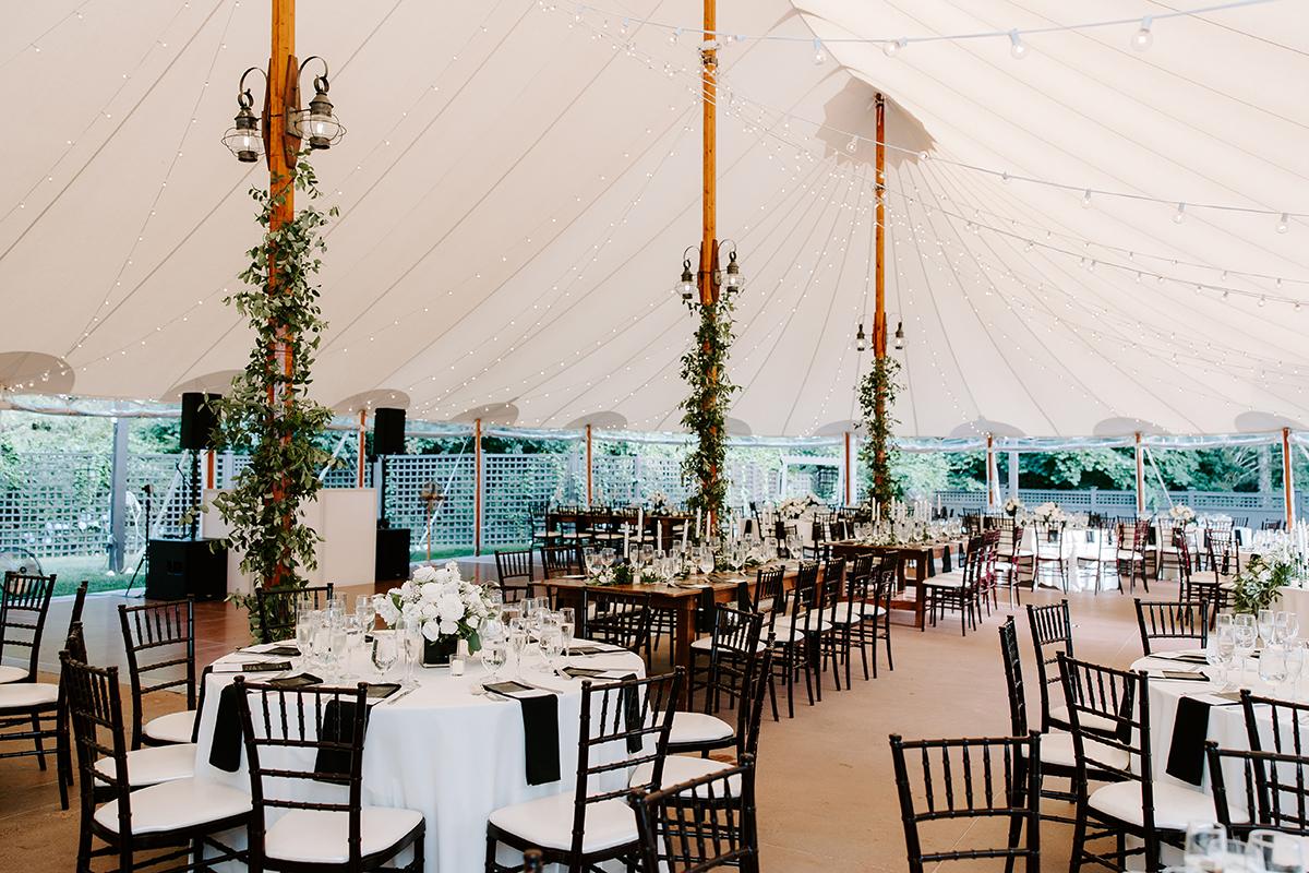 Elegant wedding reception under a tent with decorated tables and chairs.