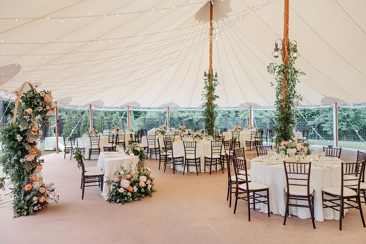 Wedding reception under a tent with tables and floral decorations.