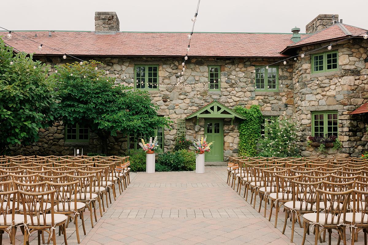 Stone building courtyard set for an outdoor wedding ceremony with wooden chairs.