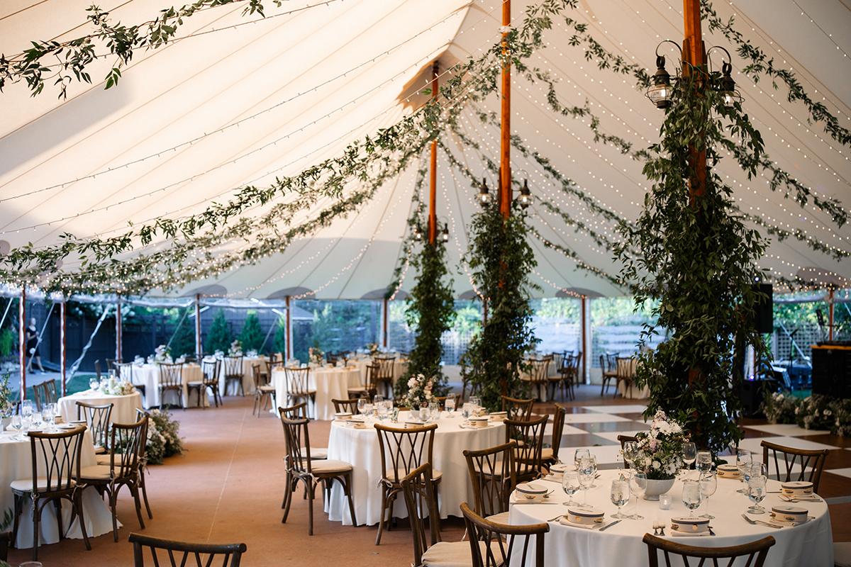 Wedding reception in a tent with draped greenery and round tables.