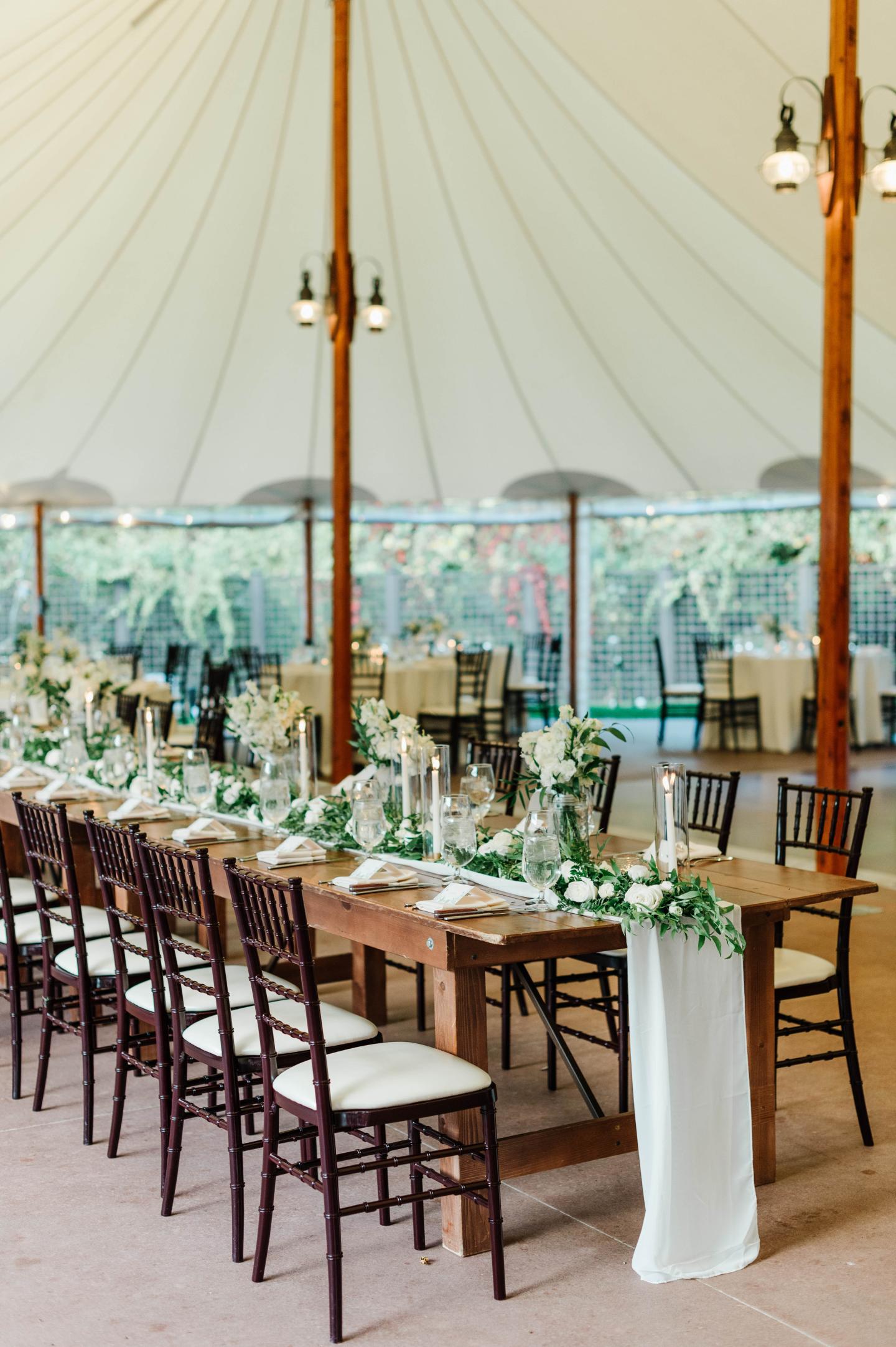Elegant wedding table under a white canopy with candles and greenery.