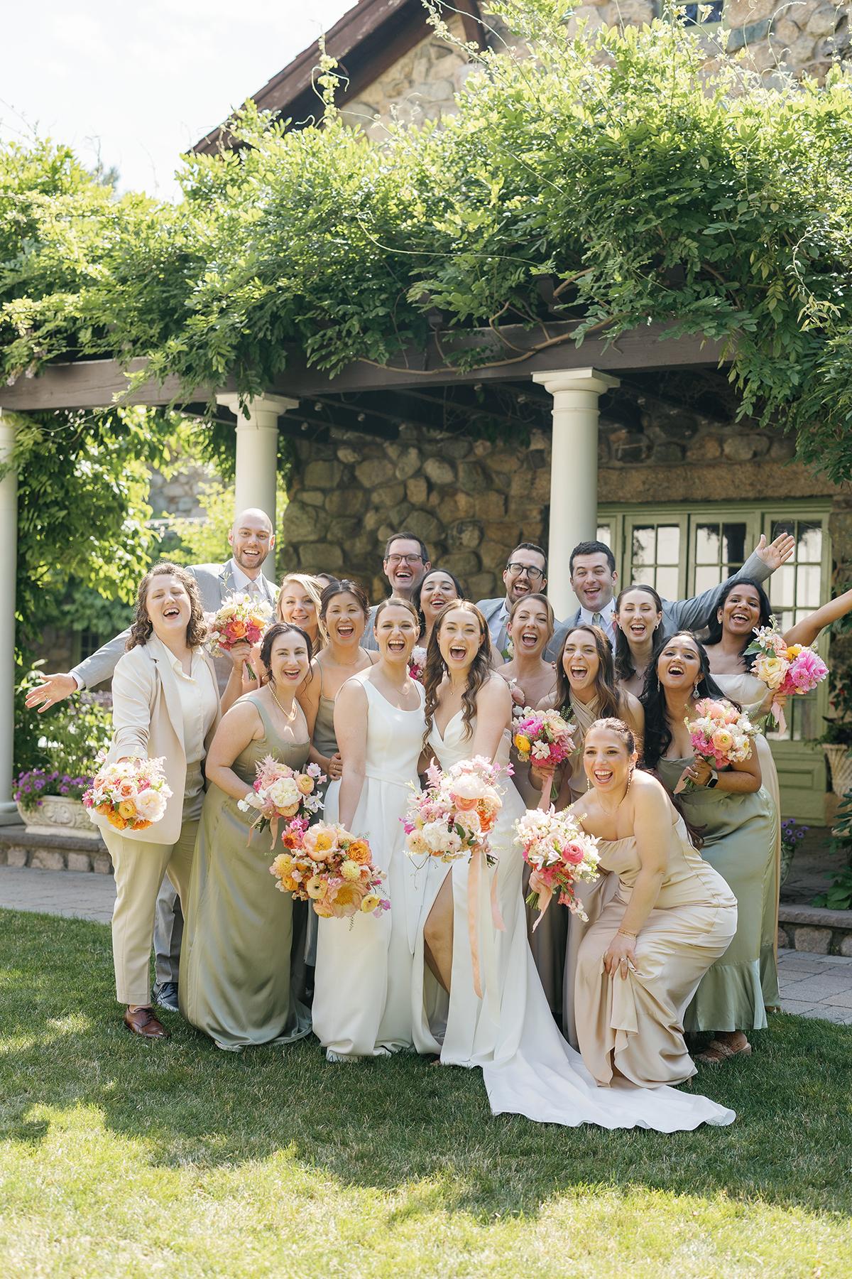 Wedding party smiling in garden, bridesmaids holding flower bouquets.