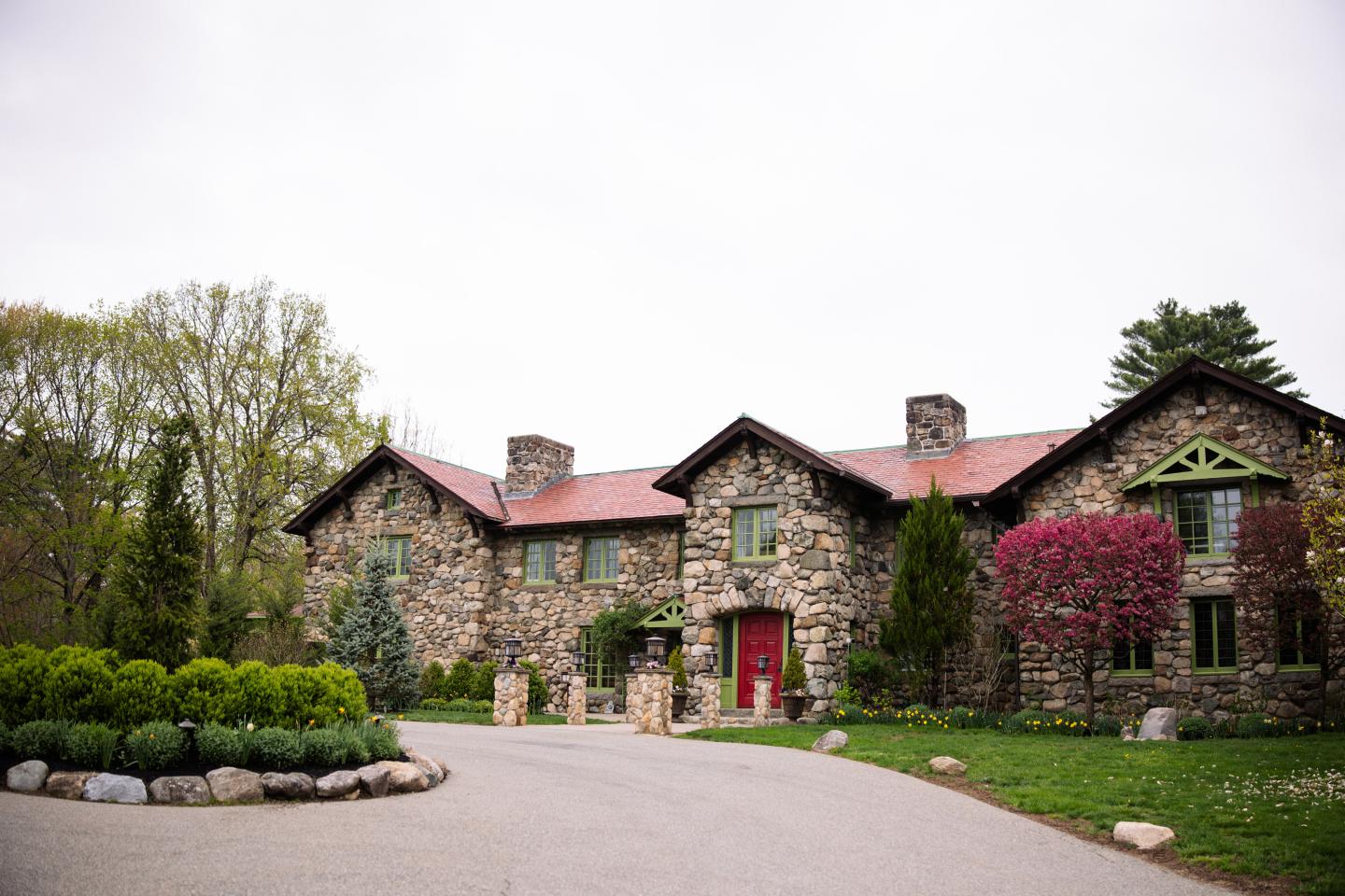 Stone house with red roof, surrounded by green trees and bushes.